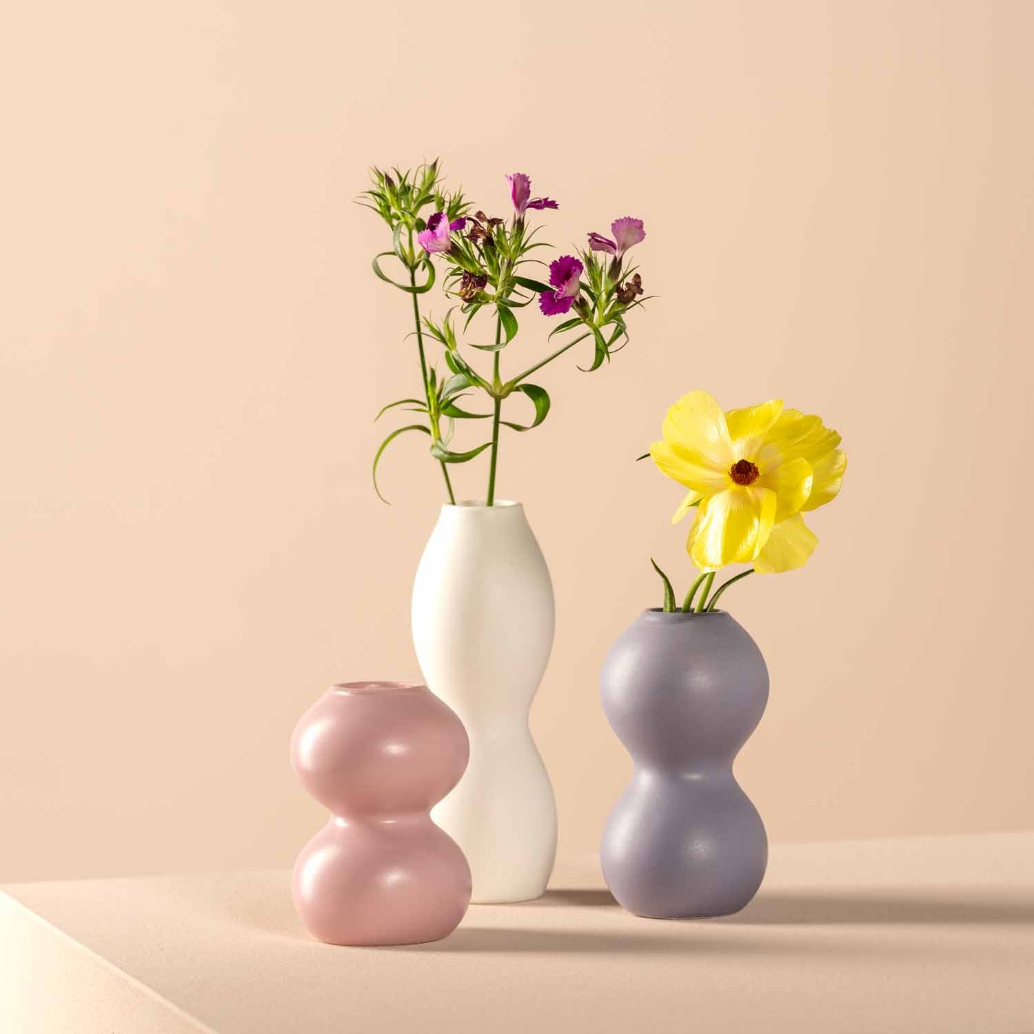 Keramikvase VIVACE in Lila neben anderen Vasen mit Blumen auf Tisch
