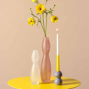 Keramikleuchter VIVACE mit gelbem Blumenstrauß und brennender Kerze auf gelbem Tisch