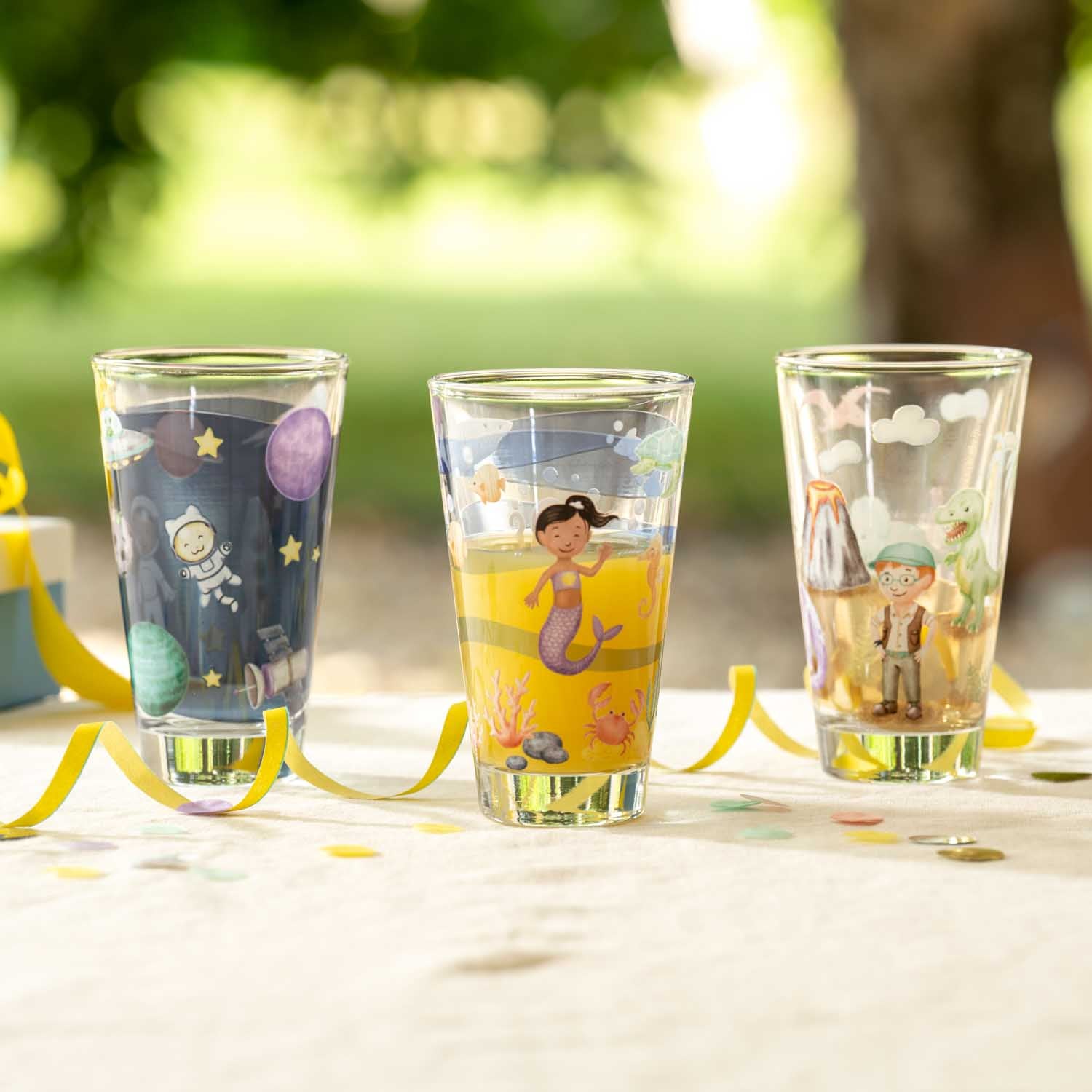 Drei Trinkgläser BAMBINI AVVENTURA mit bunten Motiven auf Gartentisch im Freien