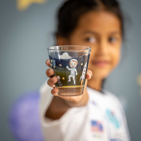Kind hält Trinkglas BAMBINI AVVENTURA mit Weltall-Motiven in die Kamera