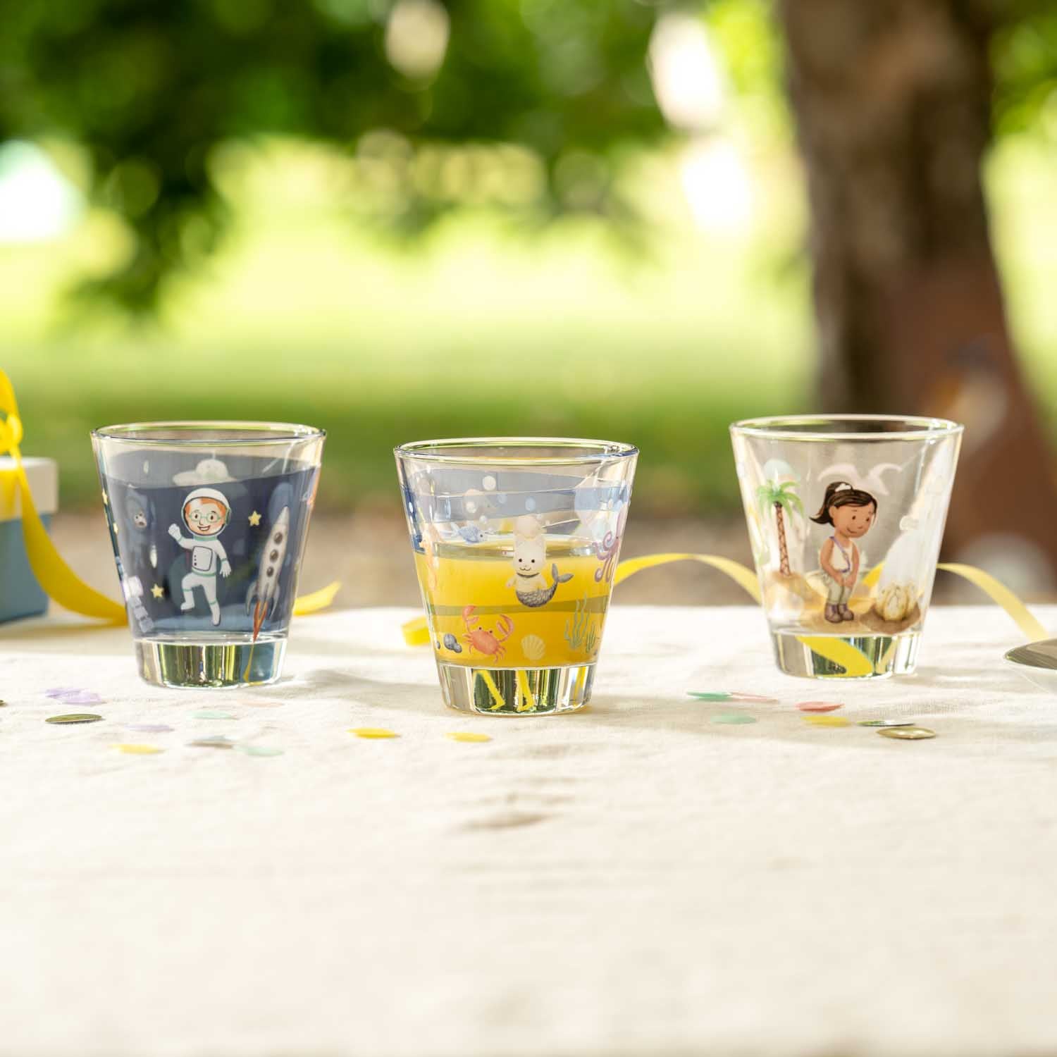 Drei Gläser mit Weltall-Motiven gefüllt mit gelber Limonade auf Gartentisch