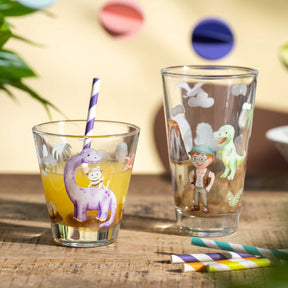 Zwei bunte Trinkgläser mit Dino-Motiven, gefüllt mit Getränken, gestreifte Trinkhalme, Holztisch