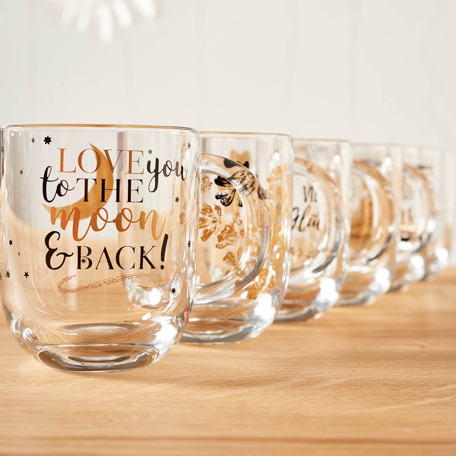Tasse EMOZIONE mit Gravur "Love you to the moon and back" auf Holztisch, mehrere Tassen nebeneinander