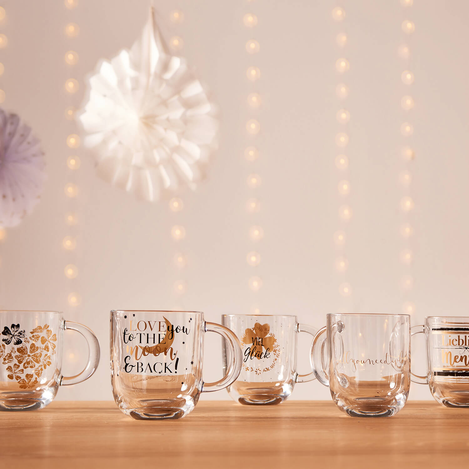 Mehrere Glastassen mit Goldverzierungen auf Holztisch, festliche Dekoration mit Lichterketten