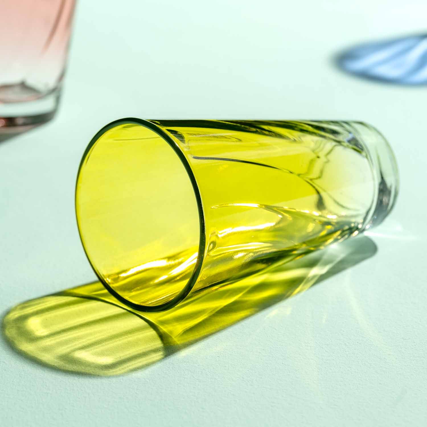 Gelbes Trinkglas TWIST umgekippt auf weißer Oberfläche mit Flüssigkeit