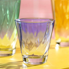 Trinkglas TWIST 215 ml in mehrfarbigem Glas auf gelbem Untergrund mit weiteren farbigen Glaesern im Hintergrund