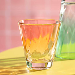 Trinkglas TWIST gefüllt mit orangegelbem Getränk auf gelbem Untergrund, rosa Hintergrund