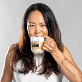 Frau trinkt aus Glastasse UFFICIO mit 'good MORNING' Gravur