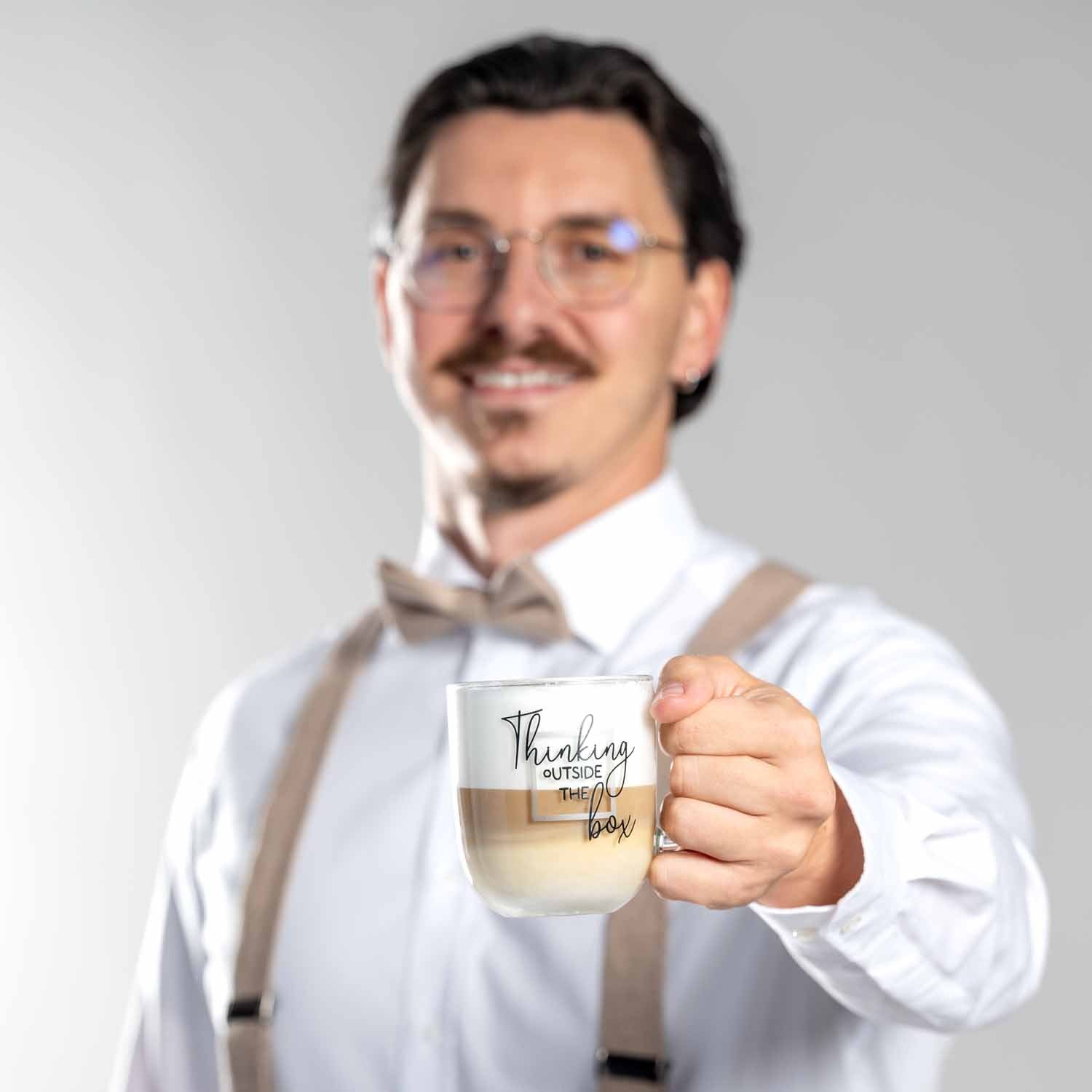 Mann in Hemd und Weste haelt Glastasse UFFICIO mit Gravur