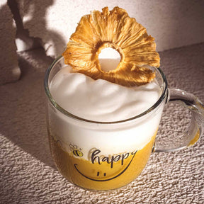 Tasse EMOZIONE mit "happy" Schriftzug, gefüllt mit Schaum, getrocknete Ananaasscheibe als Dekoration