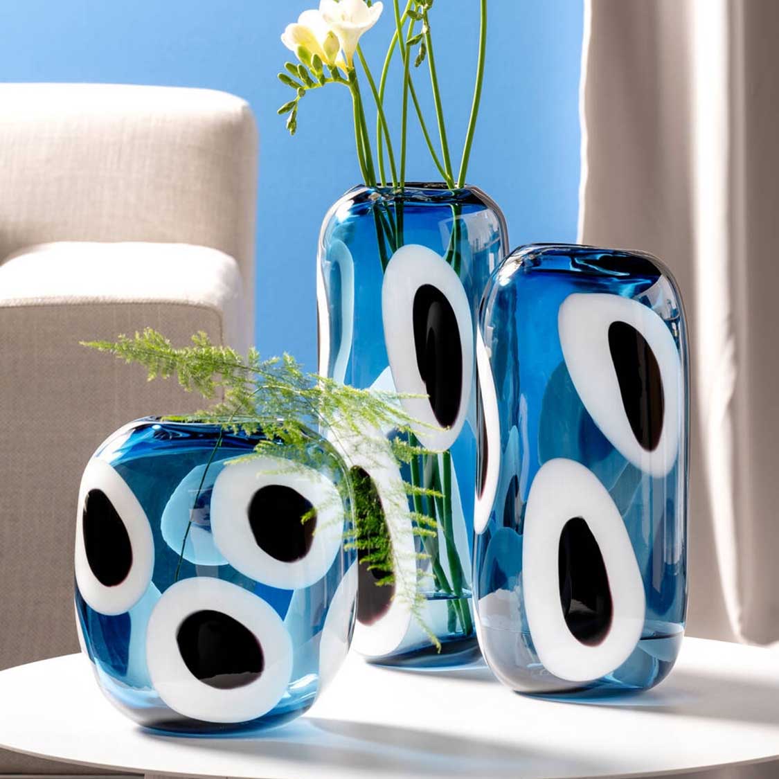 Vase OCCHI BLU in Blau mit weißen Augen-Motiven, gefüllt mit gelben Blüten und Grün