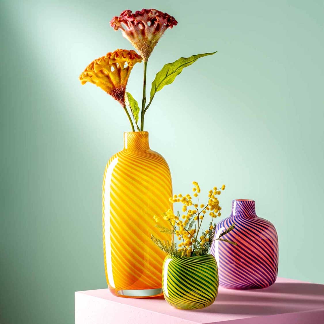 Vase FILO COLORI gelb mit bunten Nelken, daneben kleinere Vasen in Grün und Violett