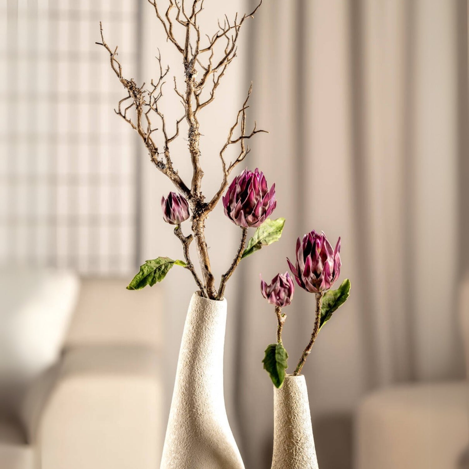Lila Artischocken FIORE in weißen Vasen mit Trockenholz, helles Wohnzimmer