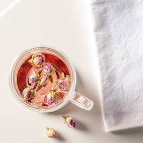 Doppelwandtasse DUO mit Rosenblütentee und getrockneten Blüten, weiße Leinenserviette