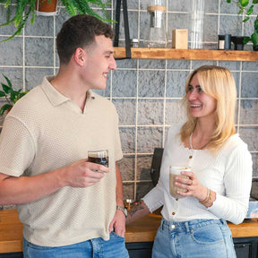 Zwei Personen halten Latte Macchiato Gläser GOCCE in moderner Wohnraum-Umgebung