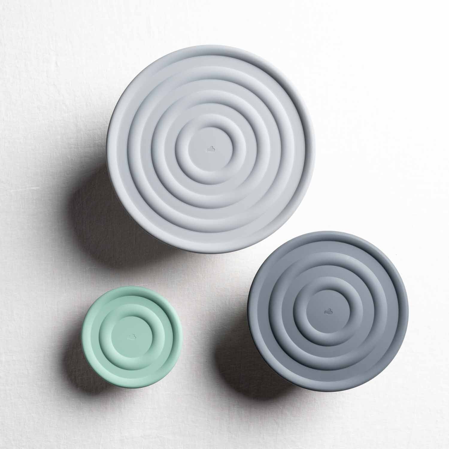Drei Silikondeckel in verschiedenen Größen und Farben, Draufsicht auf weißem Hintergrund
