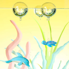 Glasskulpturen von Clownfisch und Delfin in Wasser mit Wasserpflanzen und Blasen