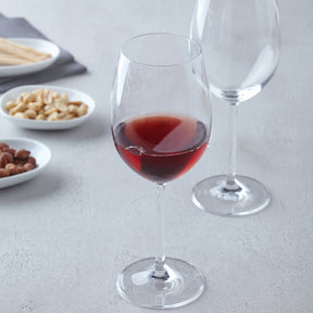 Rotweinglas DAILY gefüllt mit Rotwein, daneben leeres Glas, Nüsse und Snacks auf Tellern