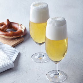 Zwei gefüllte Biergläser mit Schaum neben Brezel und Serviette