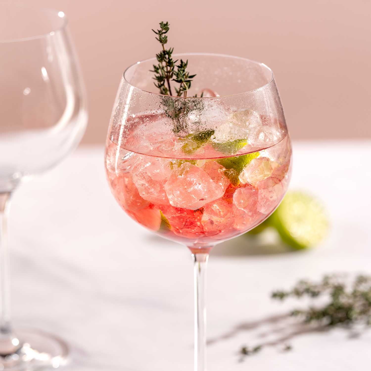 Gin Tonic Glas gefüllt mit Cocktail, Eiswürfeln, Limette und Thymian