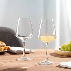 Zwei Weißweingläser PALADINO auf Holztisch, eines leer, eines mit Weißwein gefüllt, neben Obst und Servietten