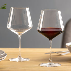 Zwei Burgundergläser PUCCINI auf Holztisch, eines mit Rotwein gefüllt