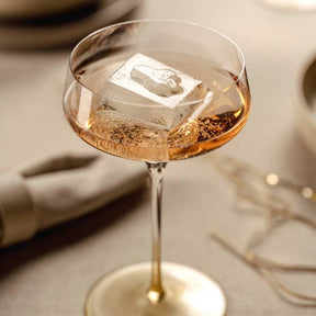 Champagnerschale PUCCINI mit goldenem Getränk und Eiswürfel auf gedecktem Tisch