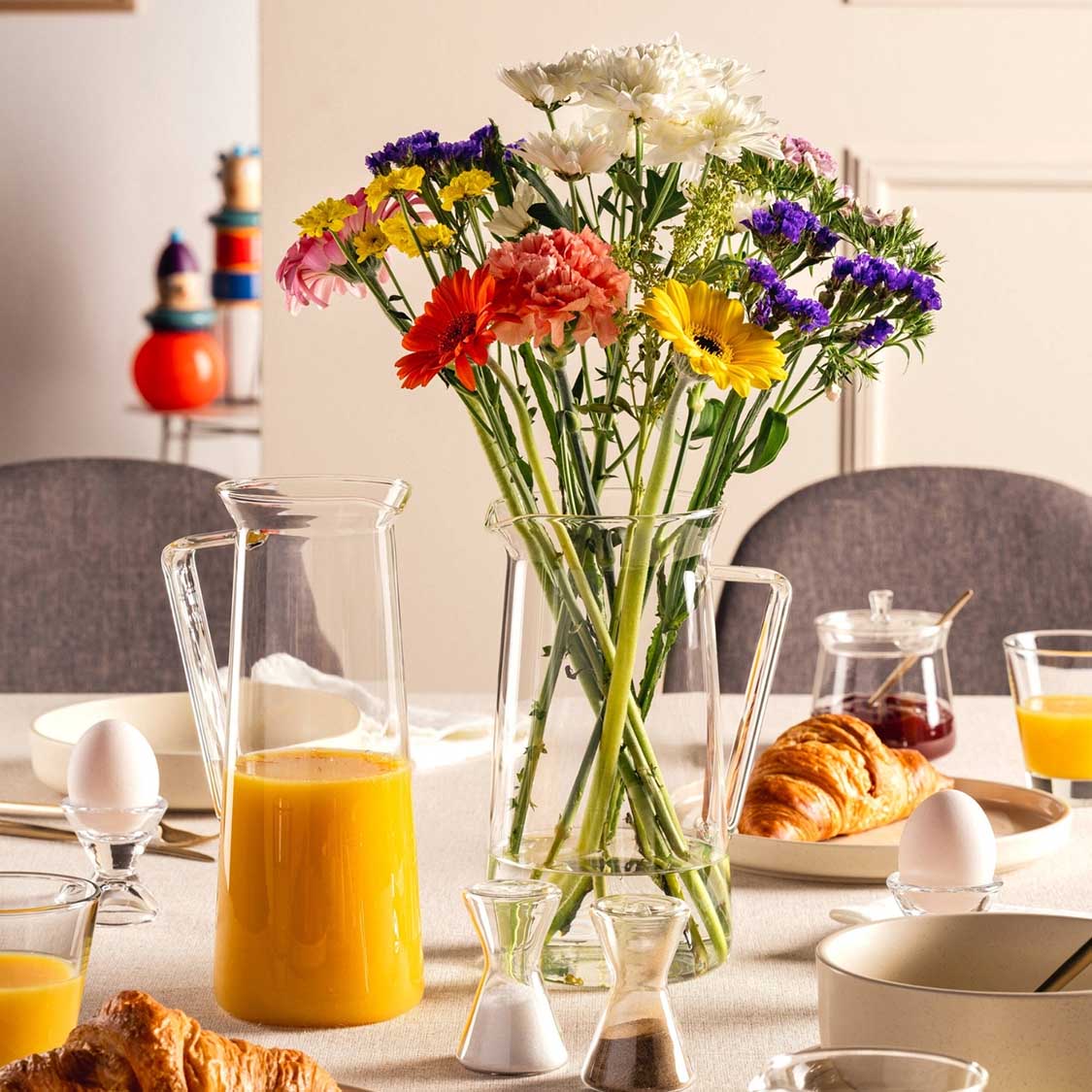 Krug GIORNO mit Orangensaft auf gedecktem Frühstückstisch mit Blumenstrauß