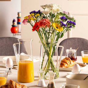 Krug GIORNO mit Orangensaft auf gedecktem Frühstückstisch mit Blumenstrauß