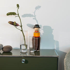 Solifleurvase mit Blumenzweigen auf grünem Sideboard, dekoriert mit Flasche und Steinen