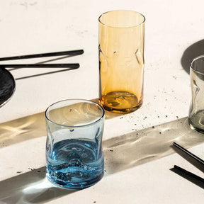 Trinkglas VESUVIO blau mit Wasser auf weißem Tisch, daneben Gläser in anderen Farben