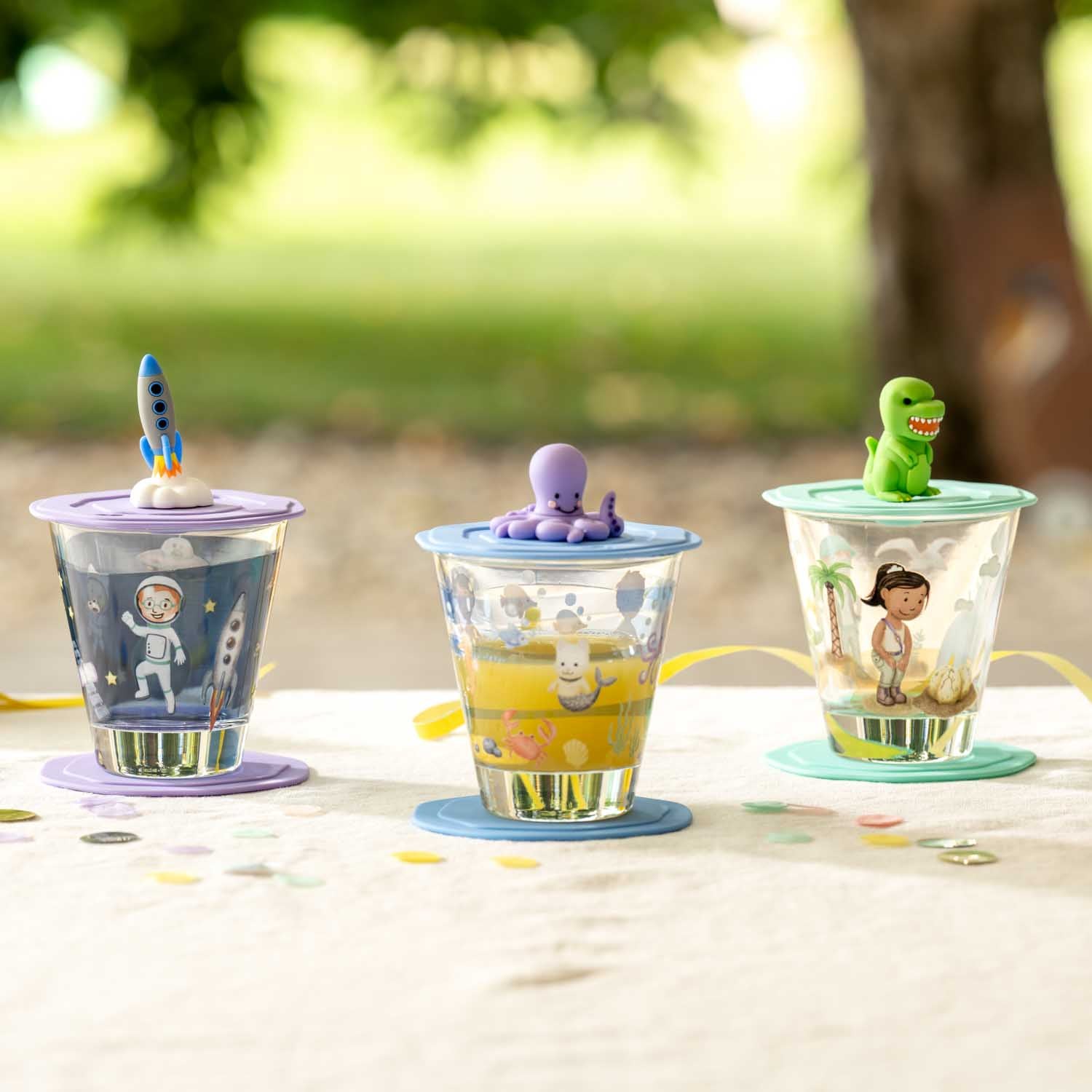 Drei Trinkbecher mit Spielzeugfiguren auf Gartentisch im Freien