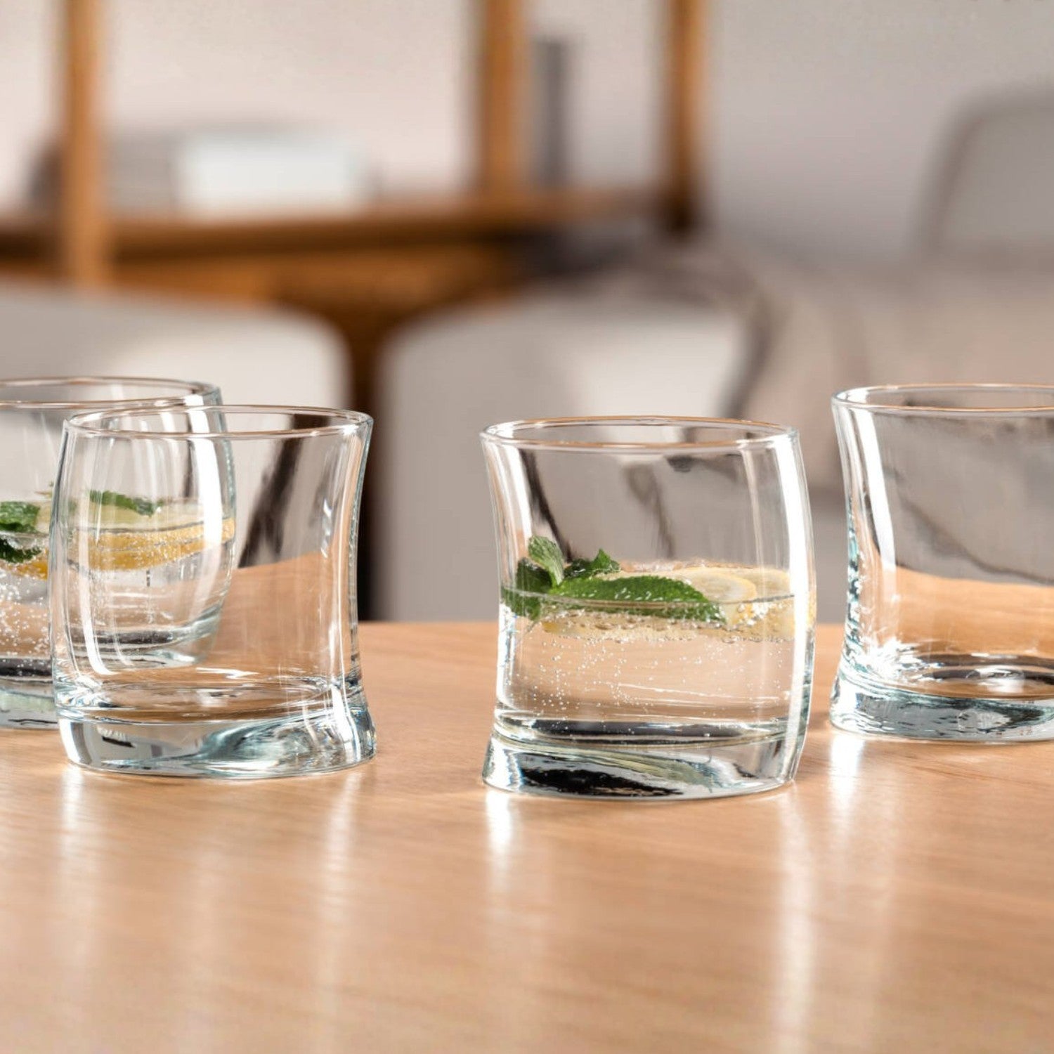 Vier Trinkgläser SWING auf Holztisch, gefüllt mit Wasser und Minze, Wohnraum im Hintergrund