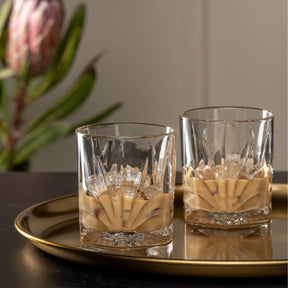 Zwei Whiskybecher CAPRI mit Kühlsteinen auf goldenem Tablett, Dekoration im Hintergrund