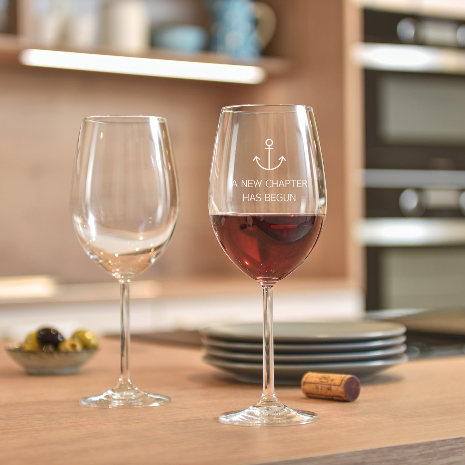 Bordeauxglas mit Gravur "A new chapter has begun" auf gedecktem Küchentisch, gefüllt mit Rotwein