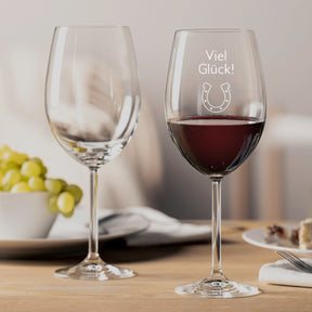 Bordeauxglas DAILY mit Gravur "Viel Glück" auf gedecktem Tisch, daneben leeres Glas und Weintrauben