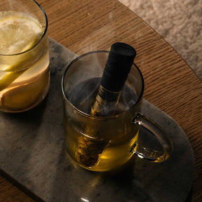 Teeglas NOVO mit Infuser auf Marmortablett, gefüllt mit Tee, daneben Glas mit Getränk