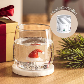 Trinkglas RIPOSO mit Wasser und Erdbeere auf Holztisch, weihnachtliche Dekoration sichtbar
