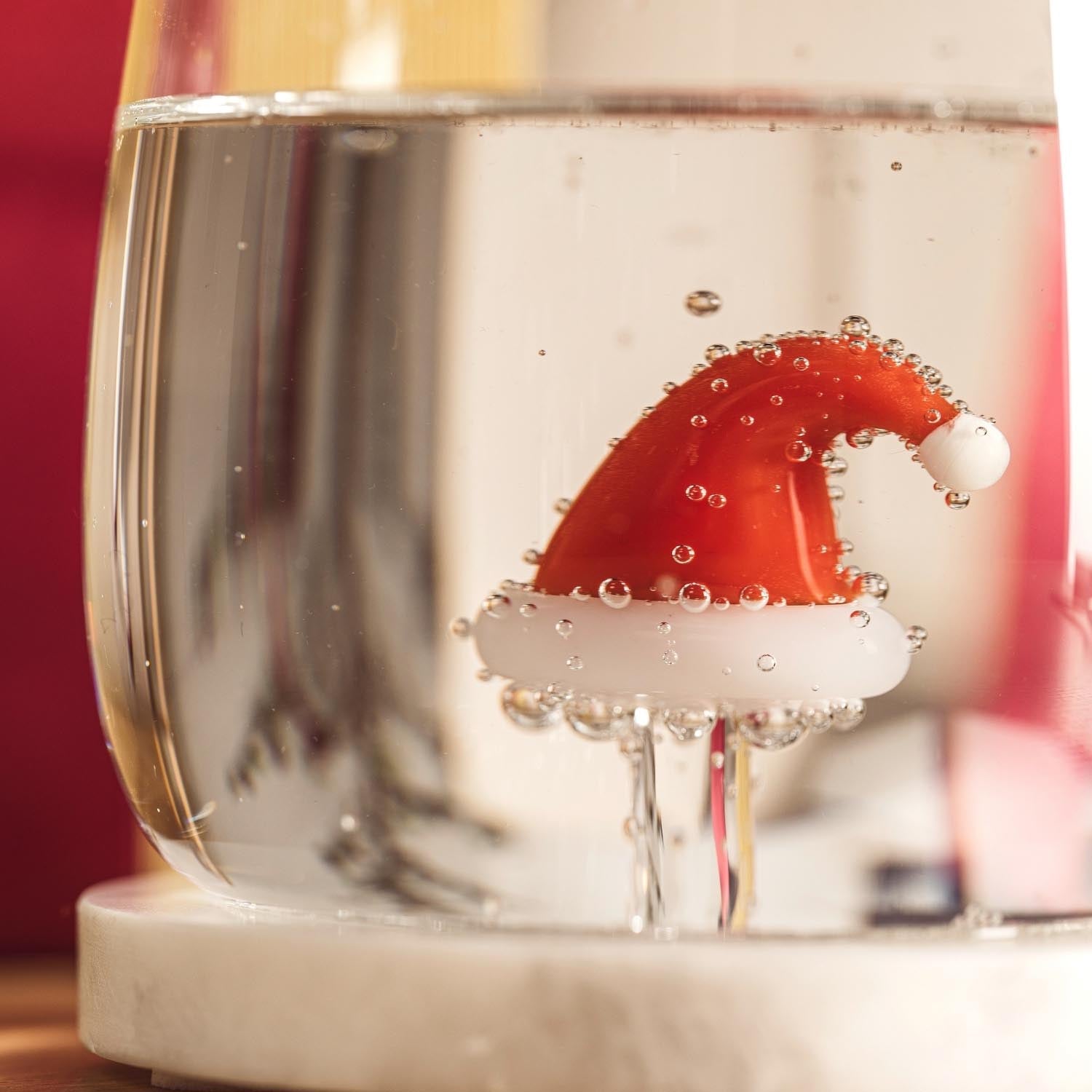 Trinkglas RIPOSO mit roter Weihnachtsmütze unter Wasser mit Blasen gefüllt