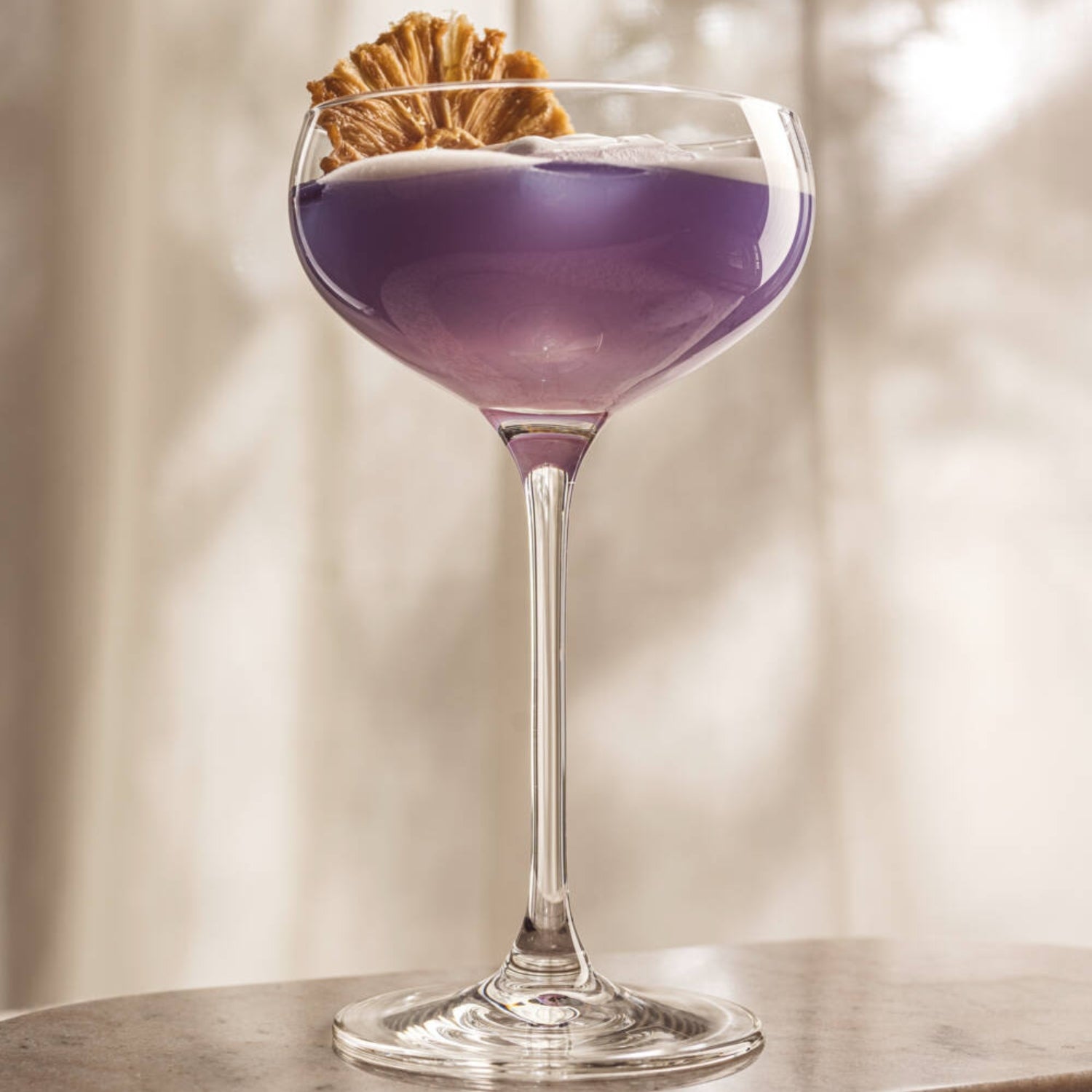 Sektschale gefüllt mit violettem Cocktail, garniert mit Trockenfrucht