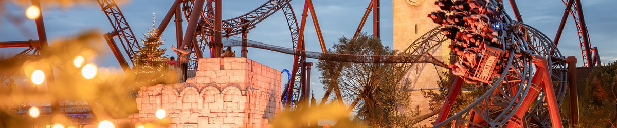 Rasante Achterbahnfahrt im Europa-Park vor malerischer Kulisse mit Uhrturm und Weihnachtsbeleuchtung in goldenem Licht.