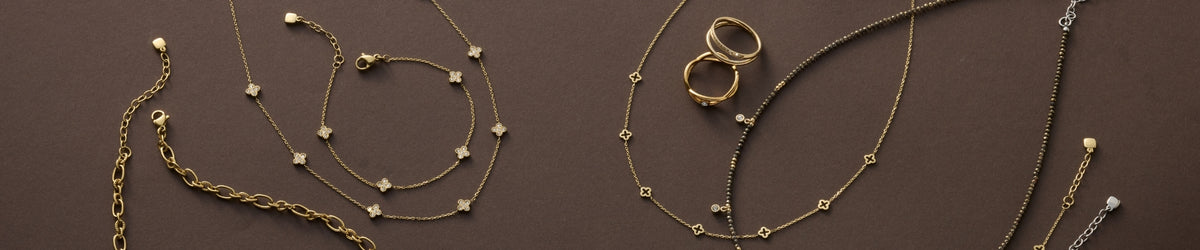 Goldene und silberne Halsketten und Ringe mit Perlen und Steinen auf braunem Hintergrund