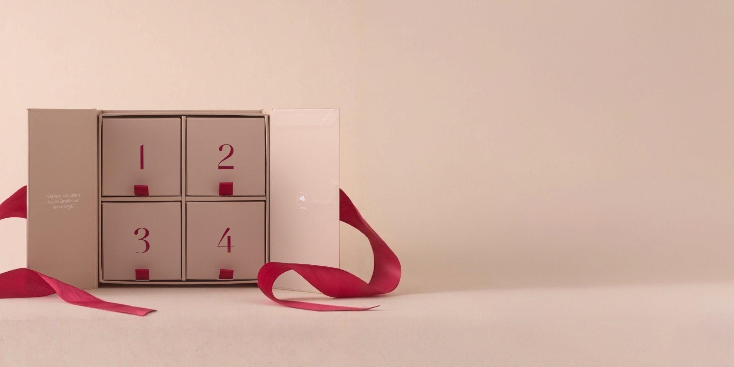 Schmuck-Adventskalender mit vier nummerierten Fächern, bordeauxrote Schleife, beige-rosafarbene Verpackung, elegante Geschenkpräsentation