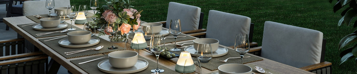 Elegant gedeckter Gartentisch mit LEONARDO Geschirr, Weingläsern, LED-Leuchten und Blumendekoration bei Abendstimmung.